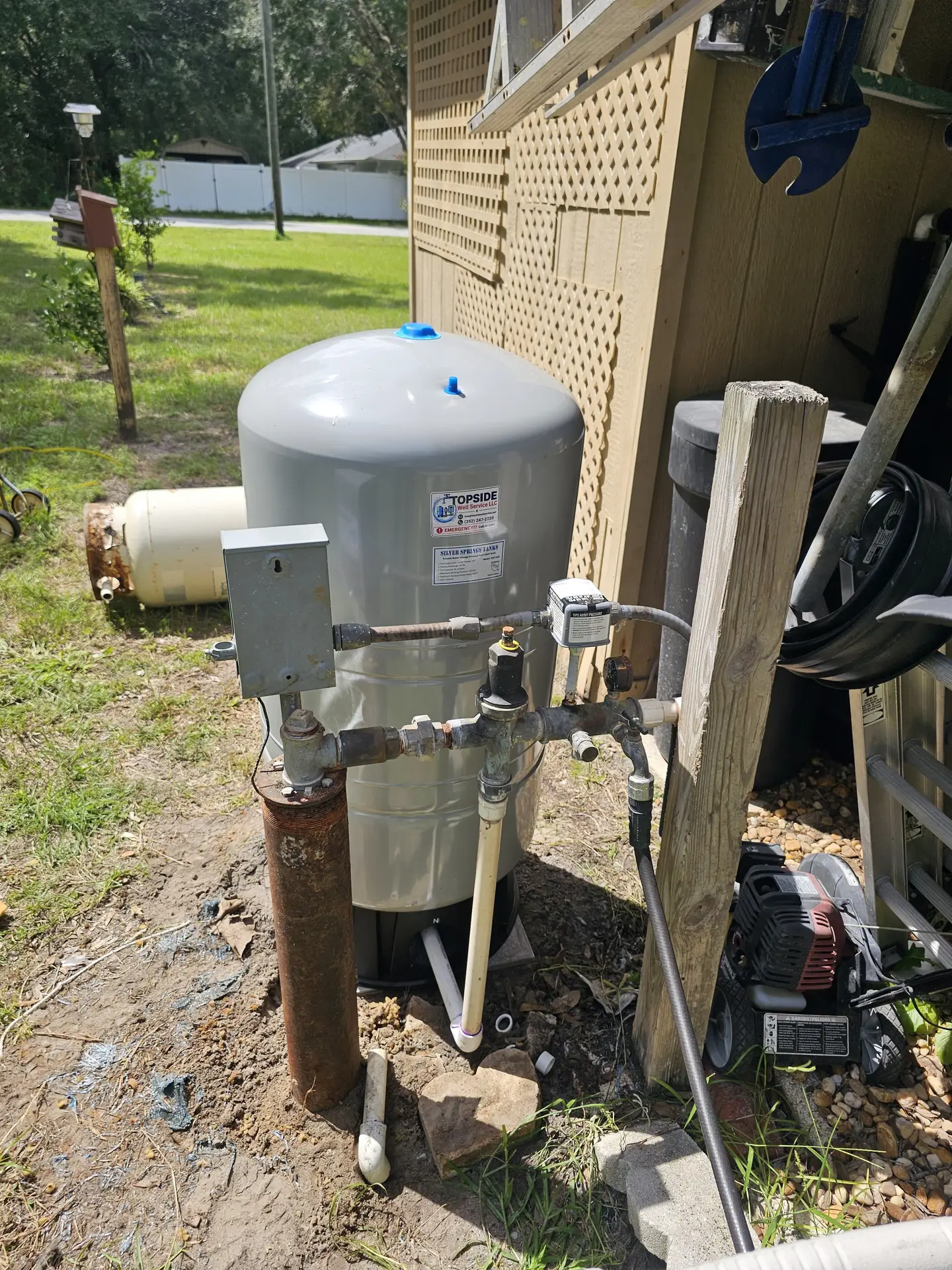 Pressure tank and wellhead piping beside a raised porch