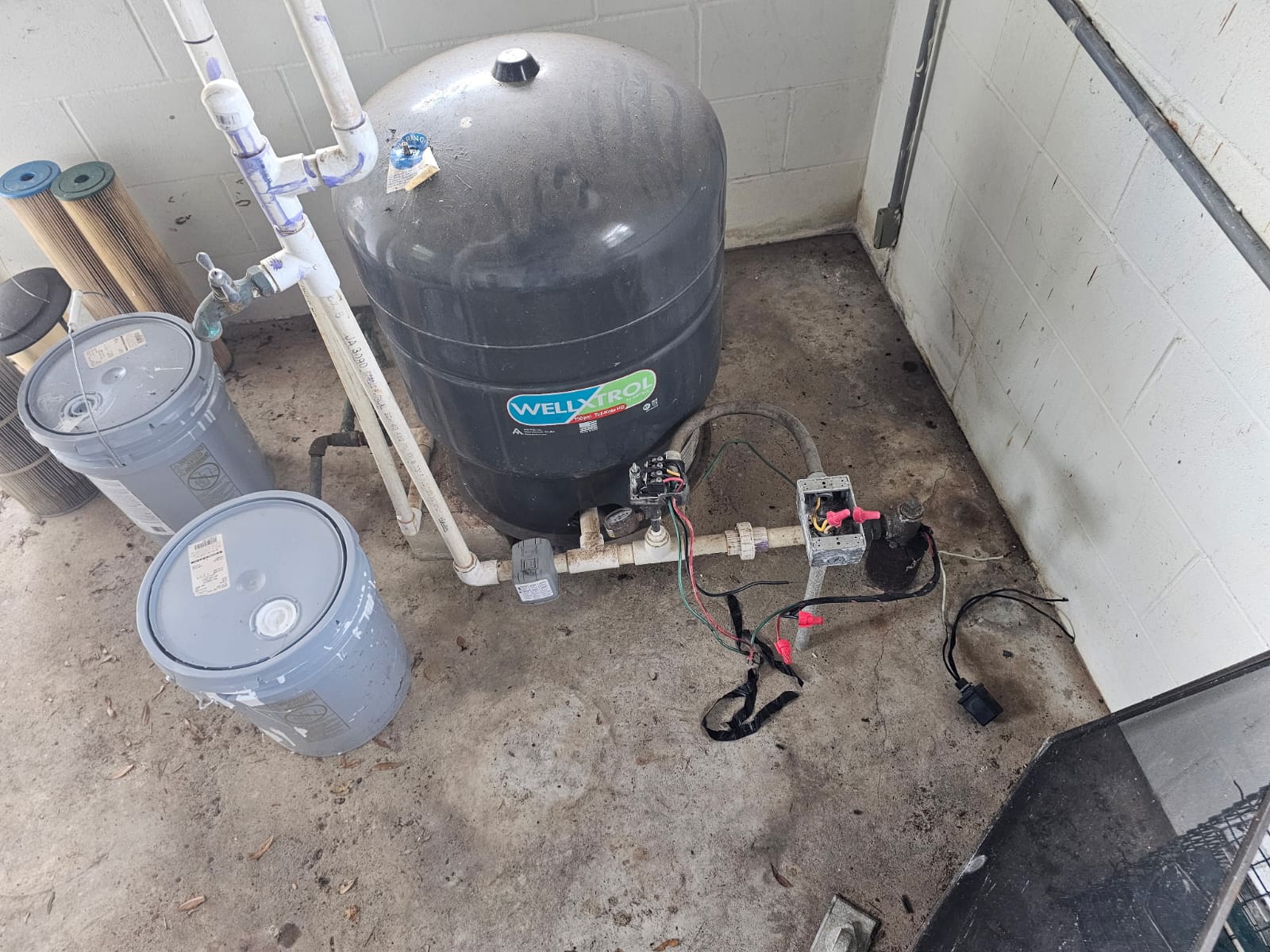 Pressure tank, PVC piping and exposed control components, with filter cartridges nearby